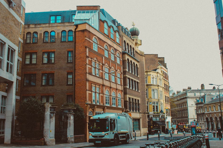 A city street scene in South Kensington featuring a row of historic, multi-storey buildings with ornate architectural details, large rectangular windows, and decorative brick and stone facades. In the