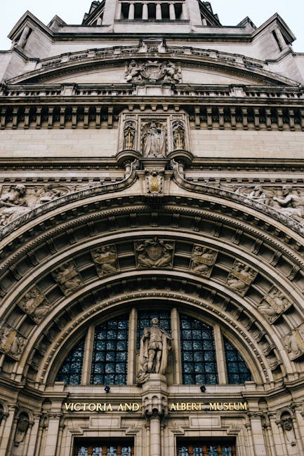 Close-up view of the detailed stone façade of the Victoria and Albert Museum, showcasing ornate architectural elements including sculpted figures, decorative arches, and intricate carvings in light g
